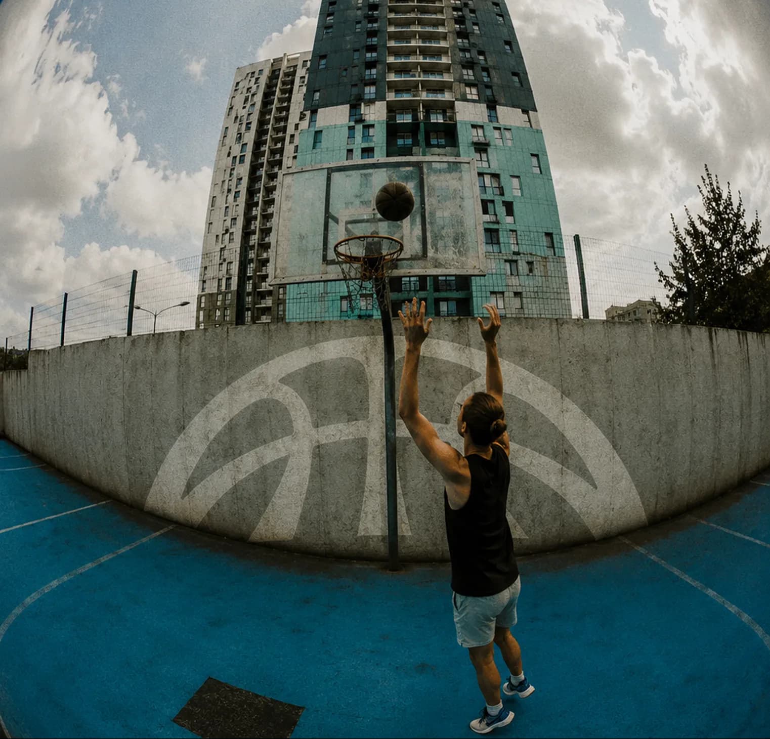 Player shooting on an outdoor court against a tower block, arc mark on the wall