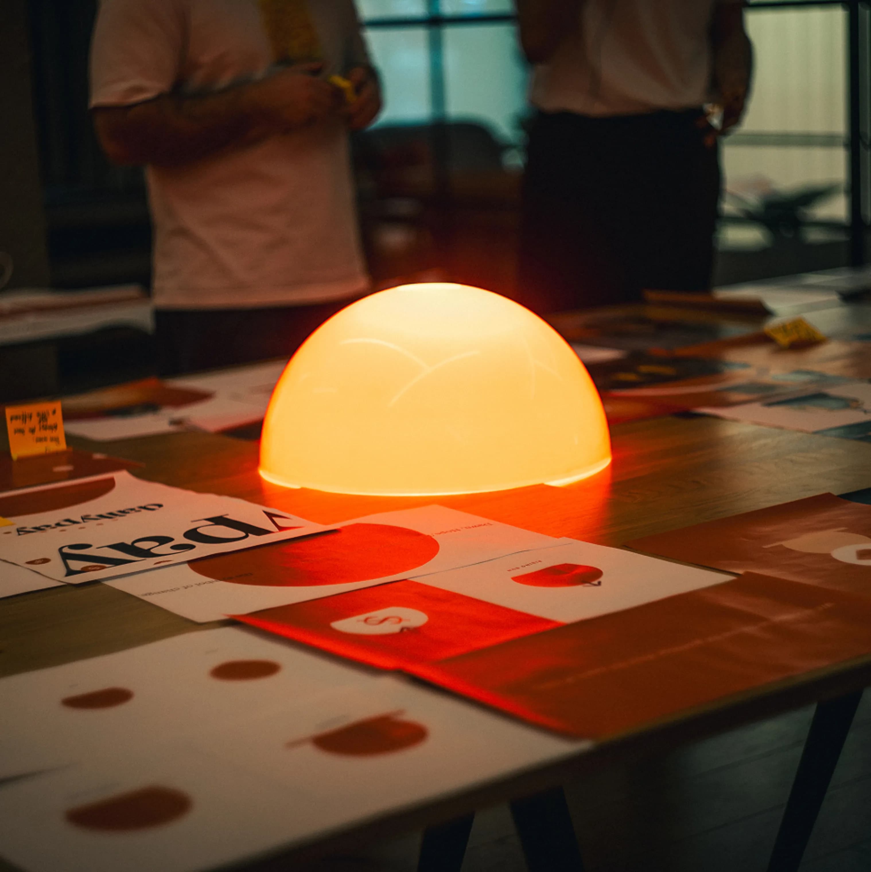 A glowing dome lamp on a studio table strewn with DailyPay print layouts