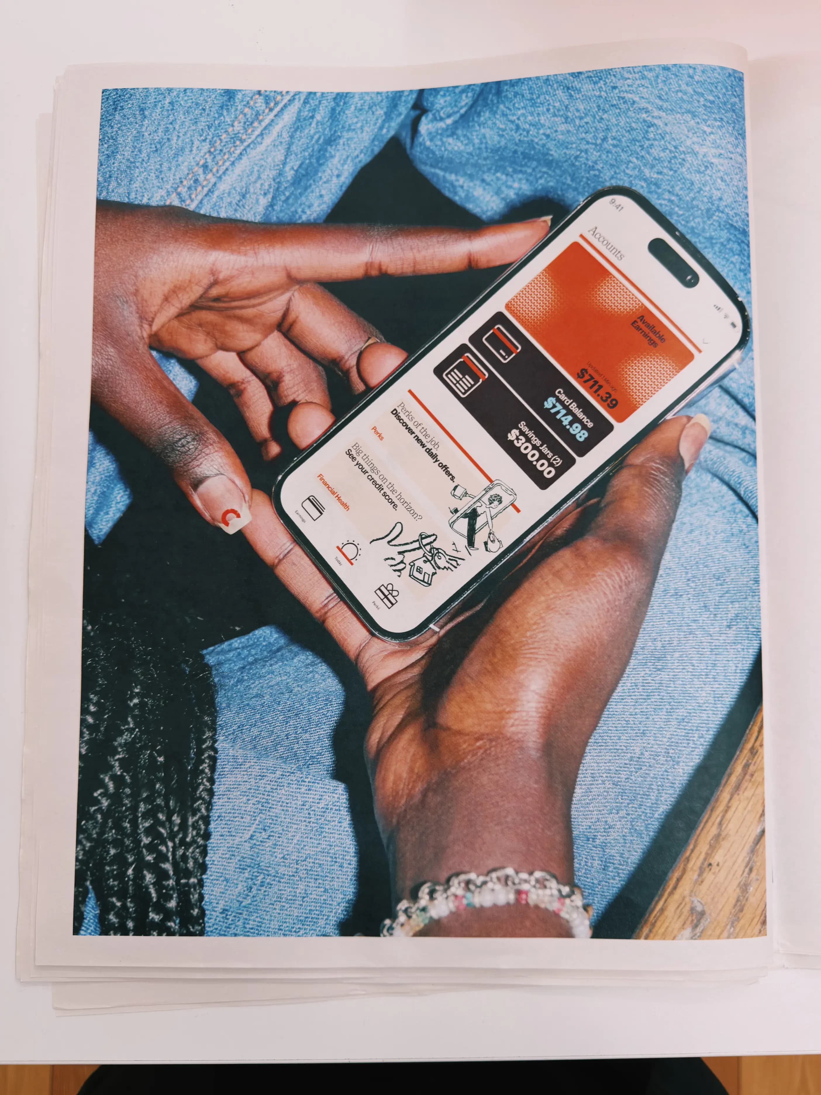 Hands holding a phone showing the DailyPay accounts screen, printed on a newspaper spread