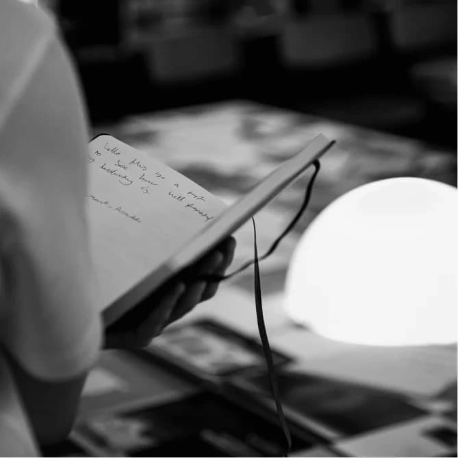 A hand holding an open notebook of handwritten notes beside a glowing lamp