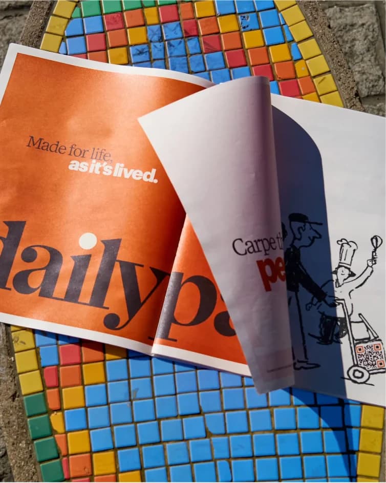 Two dailypay newspapers lying open on a coloured mosaic pavement